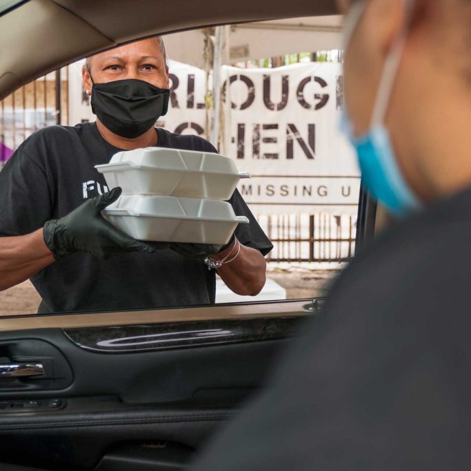 Woman in mask brings two to-go meals to man's car