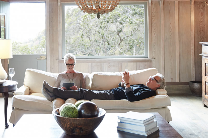55+ couple using their phone and tablet on couch
