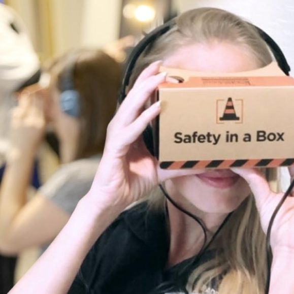Young woman with headphones looking through virtual box with Safety In A Box logo