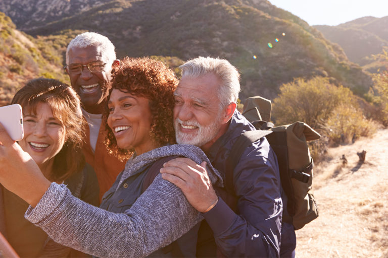 Group Of Senior Friends Posing For Selfie As They Hike Along Trail In Countryside Together.